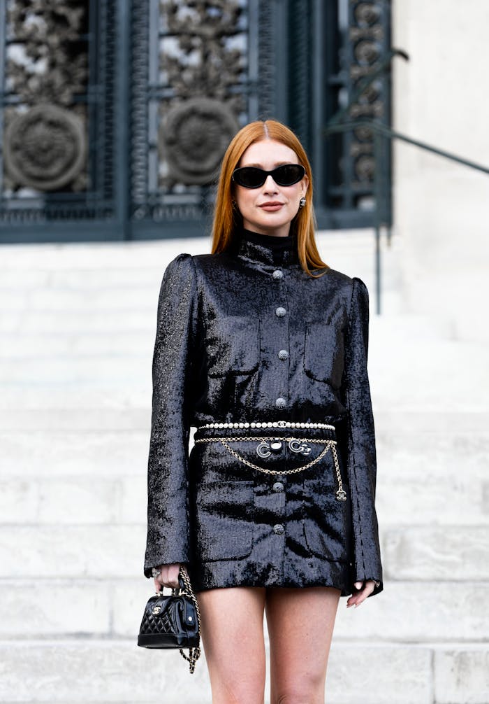 Stylish woman in black sequin dress posing on city steps with sunglasses.